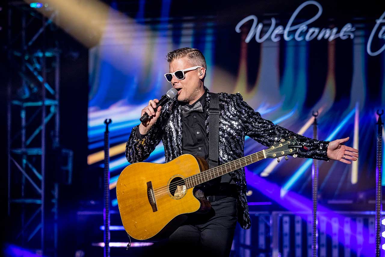 A Haygoods performer singing and playing guitar under blue stage lights